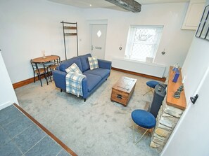 A living room with a blue sofa, a coffee table, and a dining table with chairs. - 1 bedroom accommodation in Cockermouth (Cockermouth)