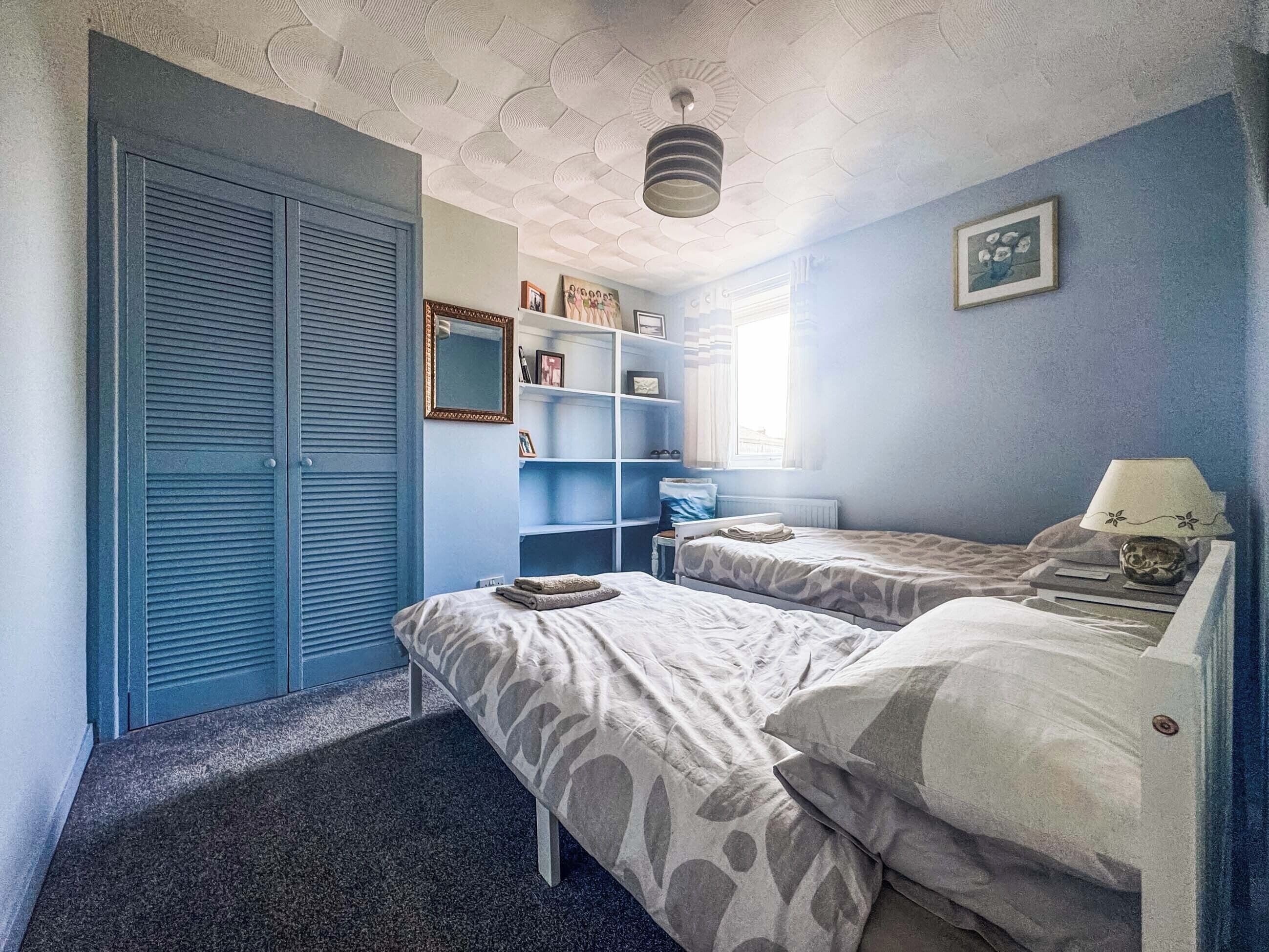 Un dormitorio con dos camas, un armario, una estantería y una ventana.