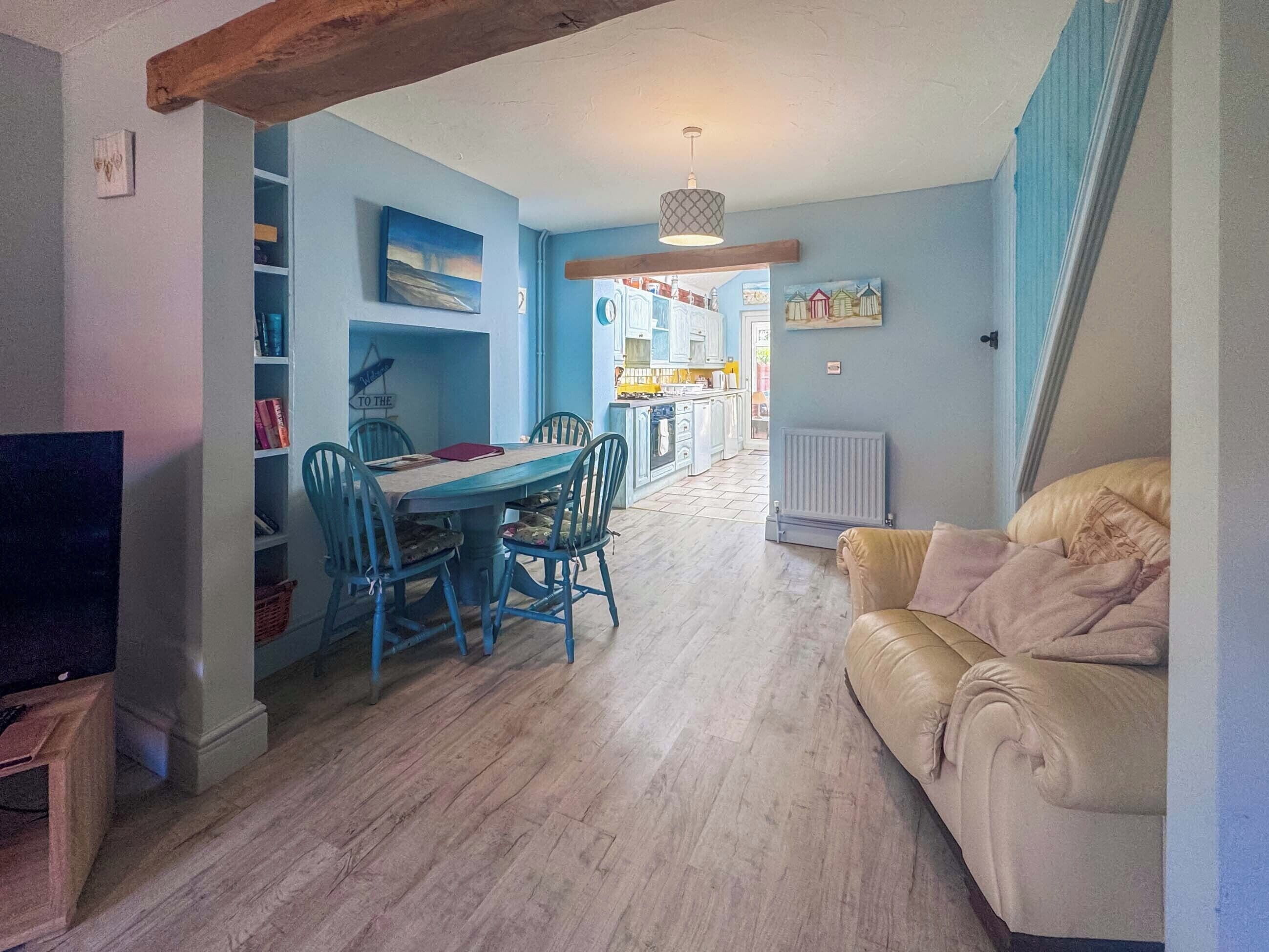 A dining area with a table and chairs, a television, and a sofa in a room with light-colored wooden flooring.