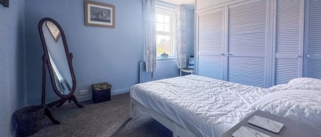 A bedroom with a bed, a dresser, a mirror, and a window with curtains.