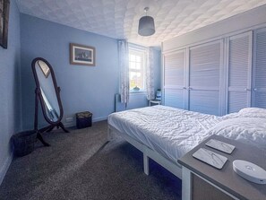 Um quarto com cama, cômoda, espelho e janela com cortinas.