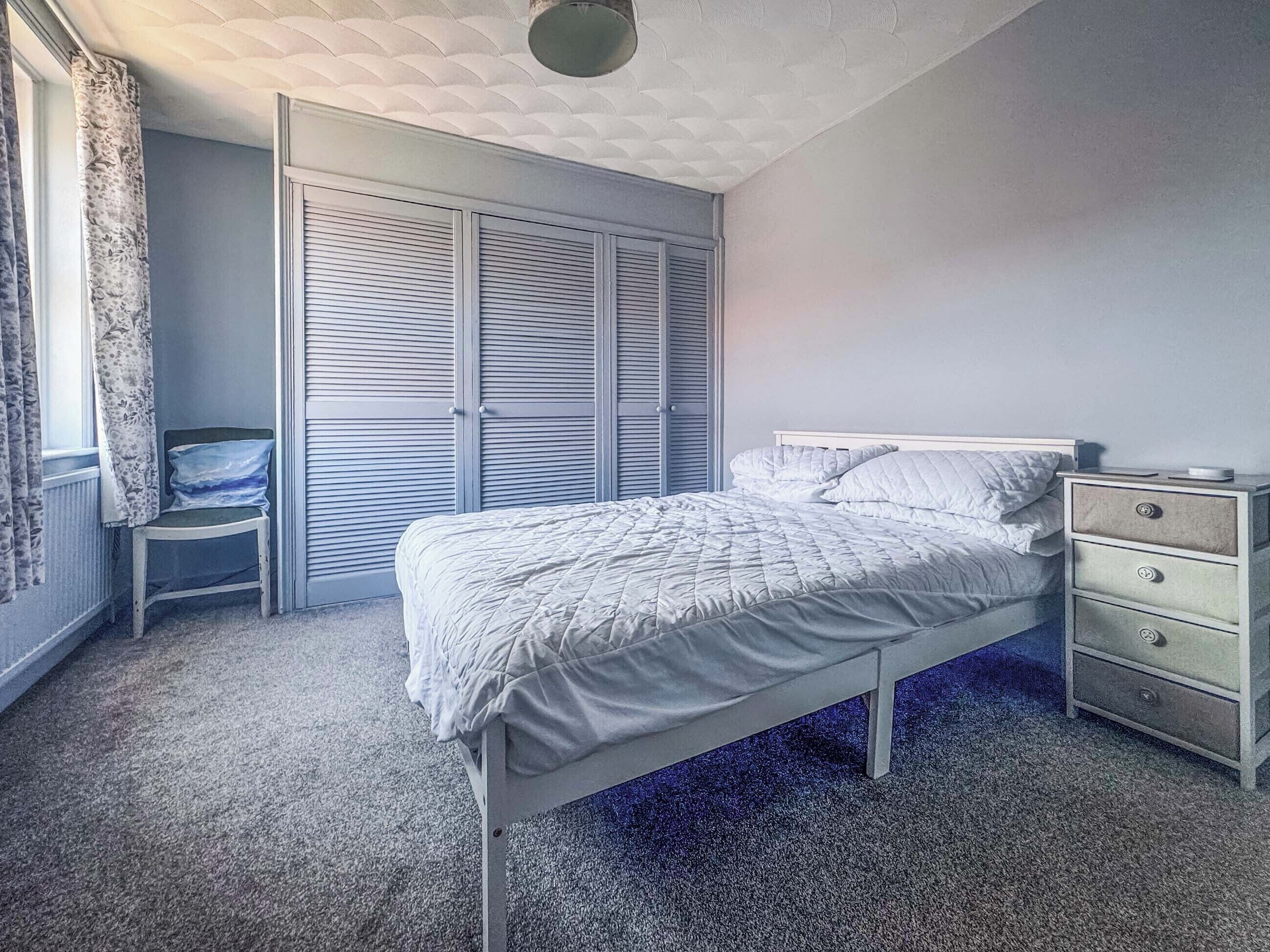 A bedroom with a bed, a nightstand, a chair, and a wardrobe.