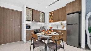 A modern kitchen with wooden cabinets, a stainless steel refrigerator, and a dining table set for four. - Feather & Stone 1BR - City Skyline (Dubai)