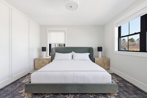 A bedroom with a large bed, two bedside tables, a window, and a door. - Luxurious NEW Home|Walk To Town & BEACH|Pool Table|Fire Pit|Bikes (Kennebunk)