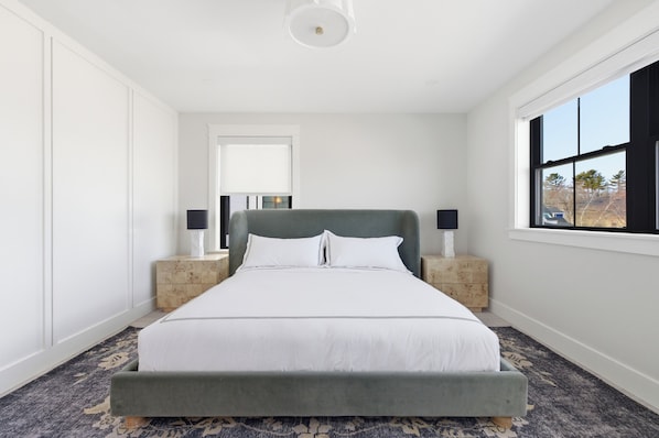 Ein Schlafzimmer mit einem großen Bett, zwei Nachttischen, einem Fenster und einer Tür.