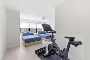 Ein modernes Schlafzimmer mit zwei Betten, einem Stehfahrrad und einem Fenster mit Blick auf Bäume.