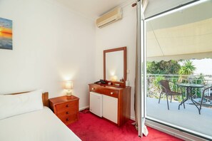 Ein Hotelzimmer mit Bett, Nachttisch, Kommode, Spiegel und einem Balkon mit Gartenmöbeln.