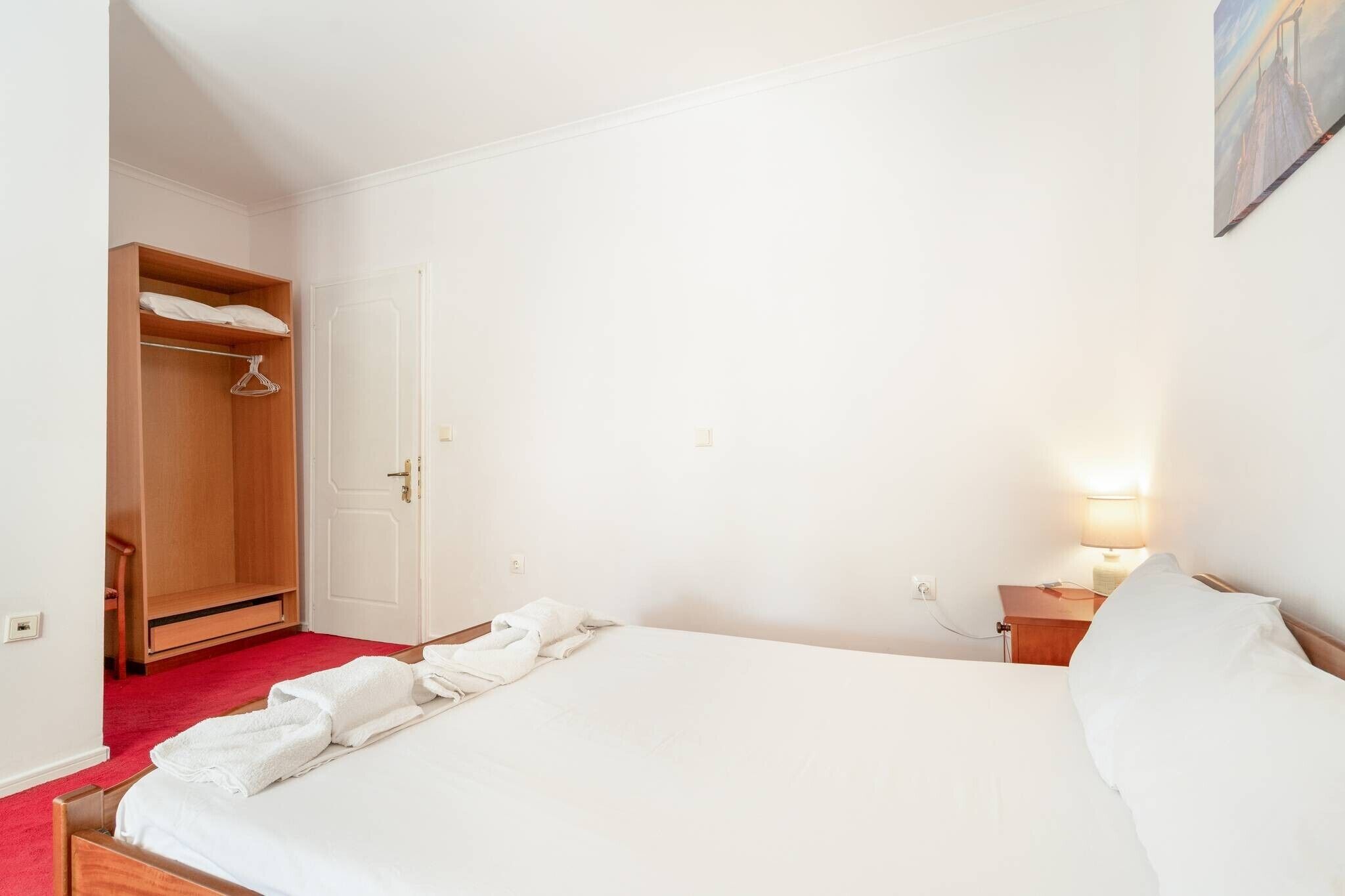 Une chambre à coucher avec un lit, une armoire, une table de chevet avec une lampe et un tableau au mur.