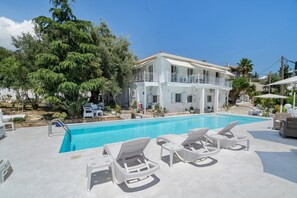 A pool area with lounge chairs, a two-story building with balconies, and surrounding greenery. - Room '1st Floor' with Sea View, Shared Pool and Wi-Fi (Nikiana)