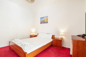 A hotel room with a wooden bed, two bedside tables with lamps, a red carpet, and a painting on the wall. - 'First Floor' Room Shared Pool and Wi-Fi (Nikiana)