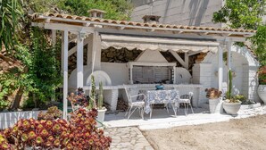 Eine Terrasse mit Grill, weißen Stühlen und Blumentöpfen.