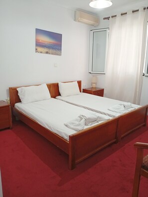 A double bed with white linens, a bedside table with a lamp, a wall-mounted air conditioner, and a painting of a sunset. - 'First Floor' Room Shared Pool and Wi-Fi (Nikiana)