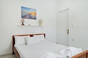 Een slaapkamer met een bed, een deur, een wandplank met een lamp en een schilderij.