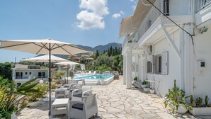A poolside area with lounge chairs and umbrellas, a stone-paved patio, and a pool. - Room 'Ground Floor' Shared Pool and Wi-Fi (Nikiana)