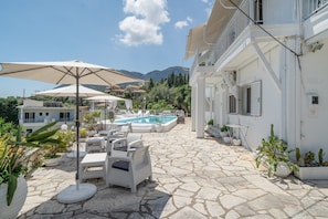 Ein Poolbereich mit Liegestühlen und Sonnenschirmen, einer terrasse aus Steinplatten und einem Schwimmbecken.