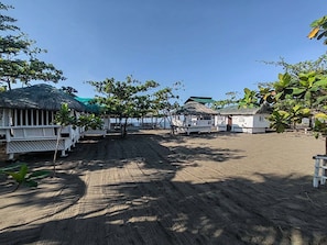 Un resort frente a la playa con cabañas de techo de paja, arena y palmeras.