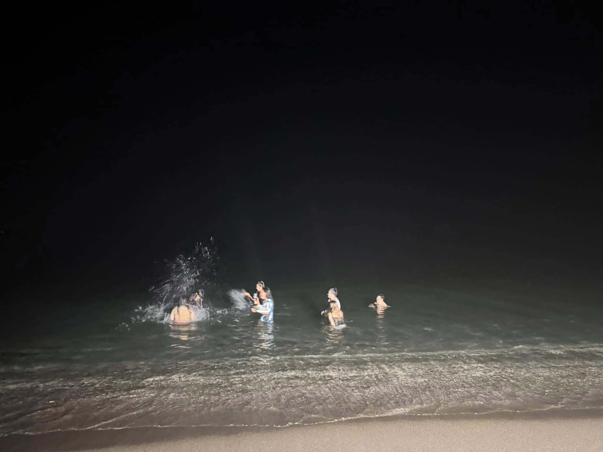 A beach scene with people in the water and a sandy shore.