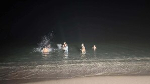 A beach scene with people in the water and a sandy shore.