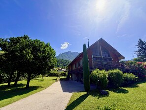 Ein Holzhaus mit geneigtem Dach, umgeben von einem gepflegten Rasen und einem Kiesweg, der zum Eingang führt.