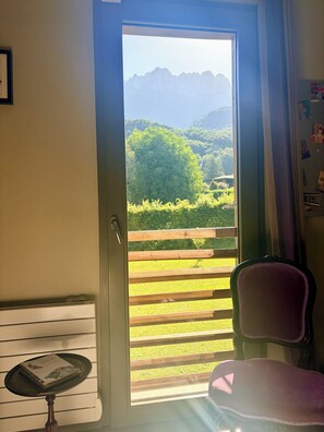 Ein Zimmer mit einer Tür, die auf einen Balkon führt, einem Sessel und einem kleinen Tisch mit einer Zeitschrift.