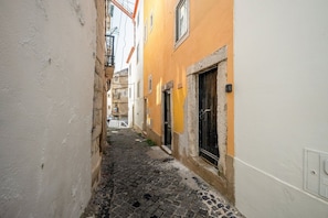 A narrow cobblestone alley between buildings with a yellow door and a black door. - GuestReady - Studio in the Heart of Alfama (Lisbon)