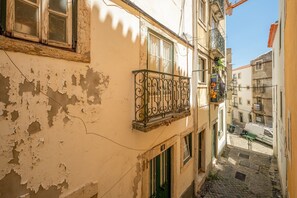 A narrow street with buildings on either side, a balcony with a wrought iron railing, and a cobblestone path. - GuestReady - Studio in the Heart of Alfama (Lisbon)