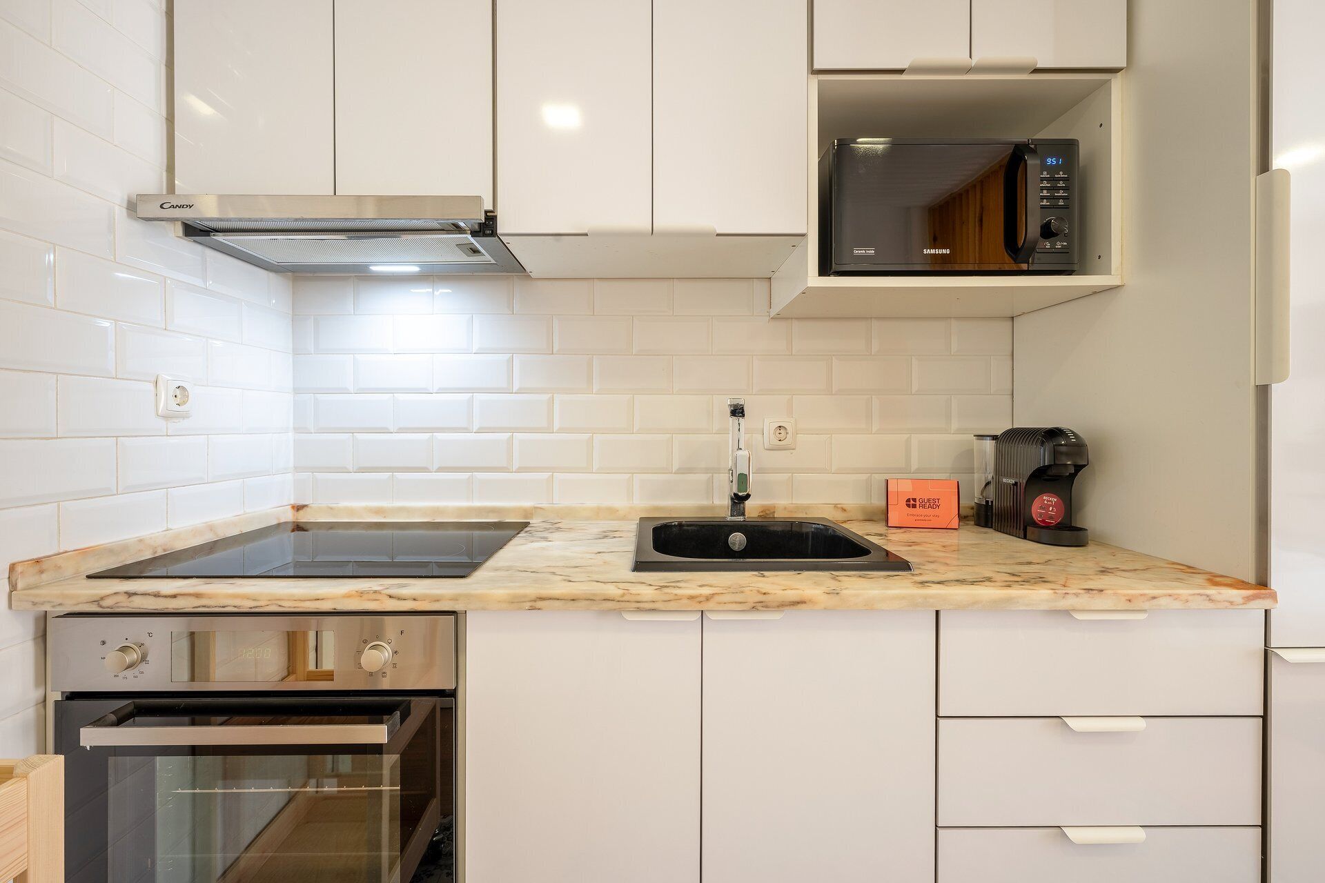 A modern kitchen with white cabinetry, a built-in microwave, a coffee machine, and a stainless steel oven.