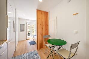 A compact living space with a kitchenette, a dining area with a green table and two chairs, and a wooden partition. - GuestReady - Studio in the Heart of Alfama (Lisbon)