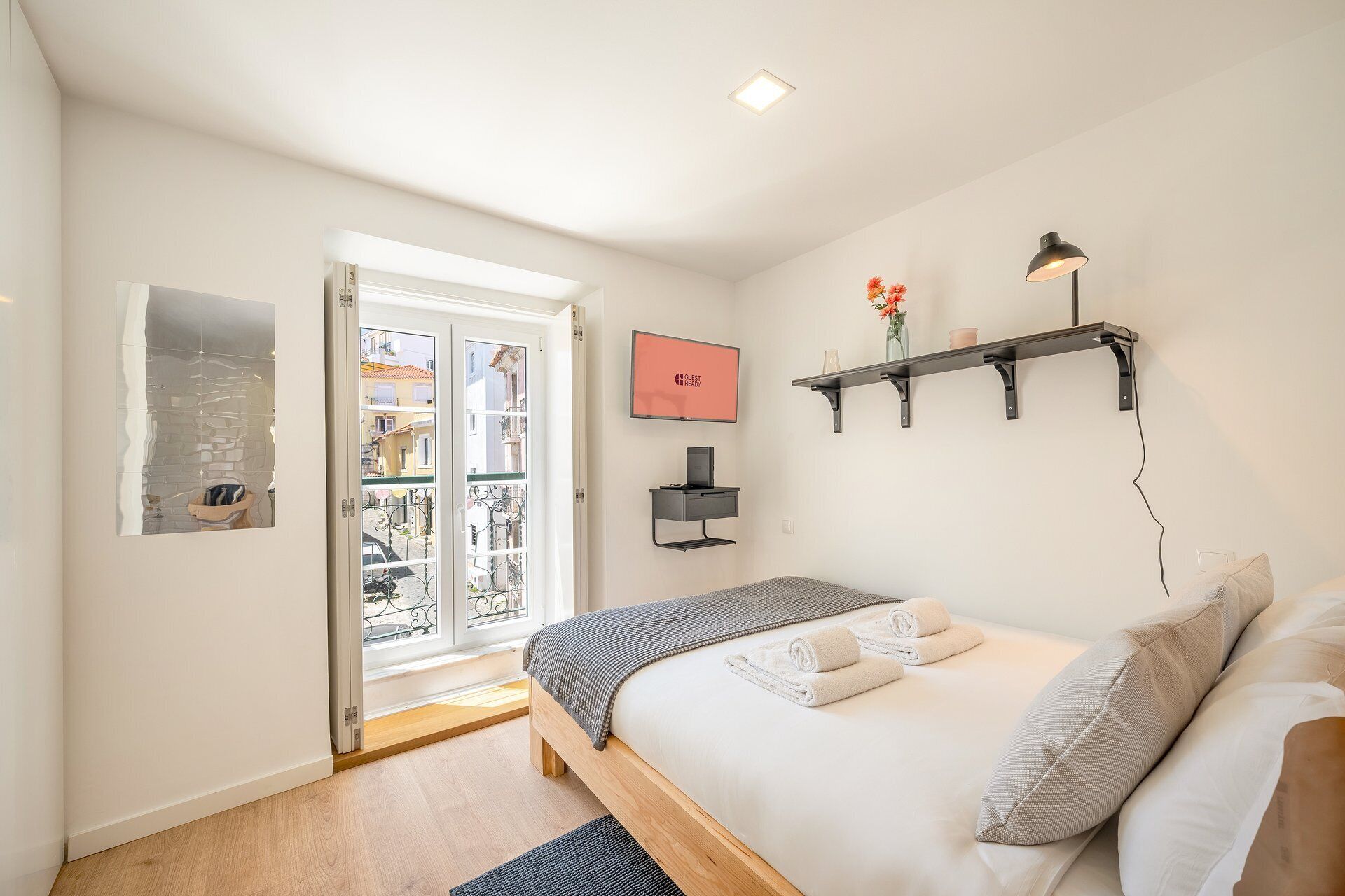Ein Schlafzimmer mit einem Bett, einem Fernseher, einem Regal und einer Tür, die auf einen Balkon führt.