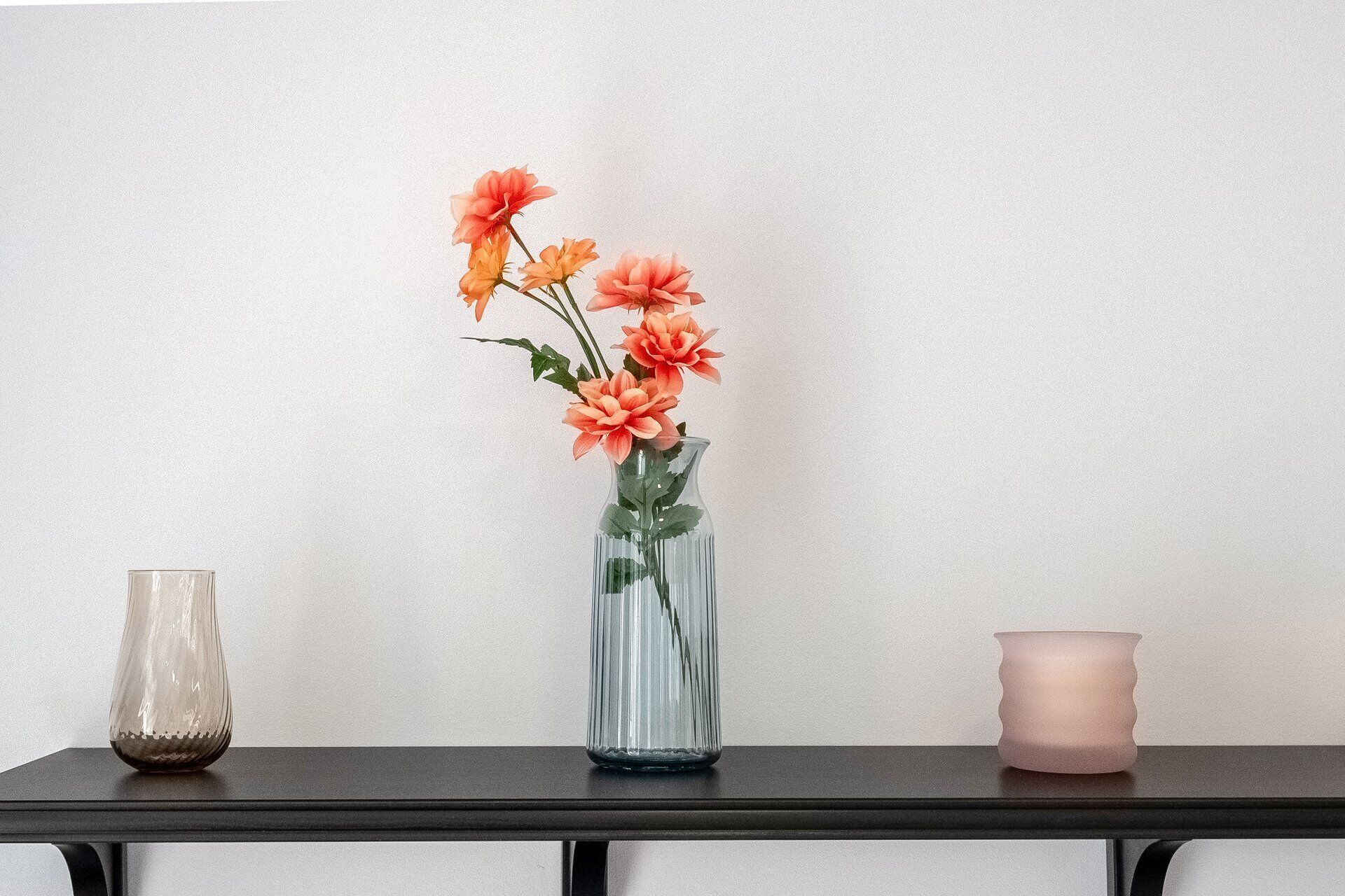 A table with a clear glass vase containing orange flowers, a smaller clear vase, and a pink candle.