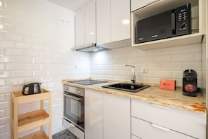 A modern kitchen with white cabinetry, a built-in microwave, a coffee maker, and a kettle on a wooden shelf. - GuestReady - Studio in the Heart of Alfama (Lisbon)
