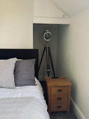 A bedroom with a bed, a bedside table with drawers, a lamp, and a small wooden stool.