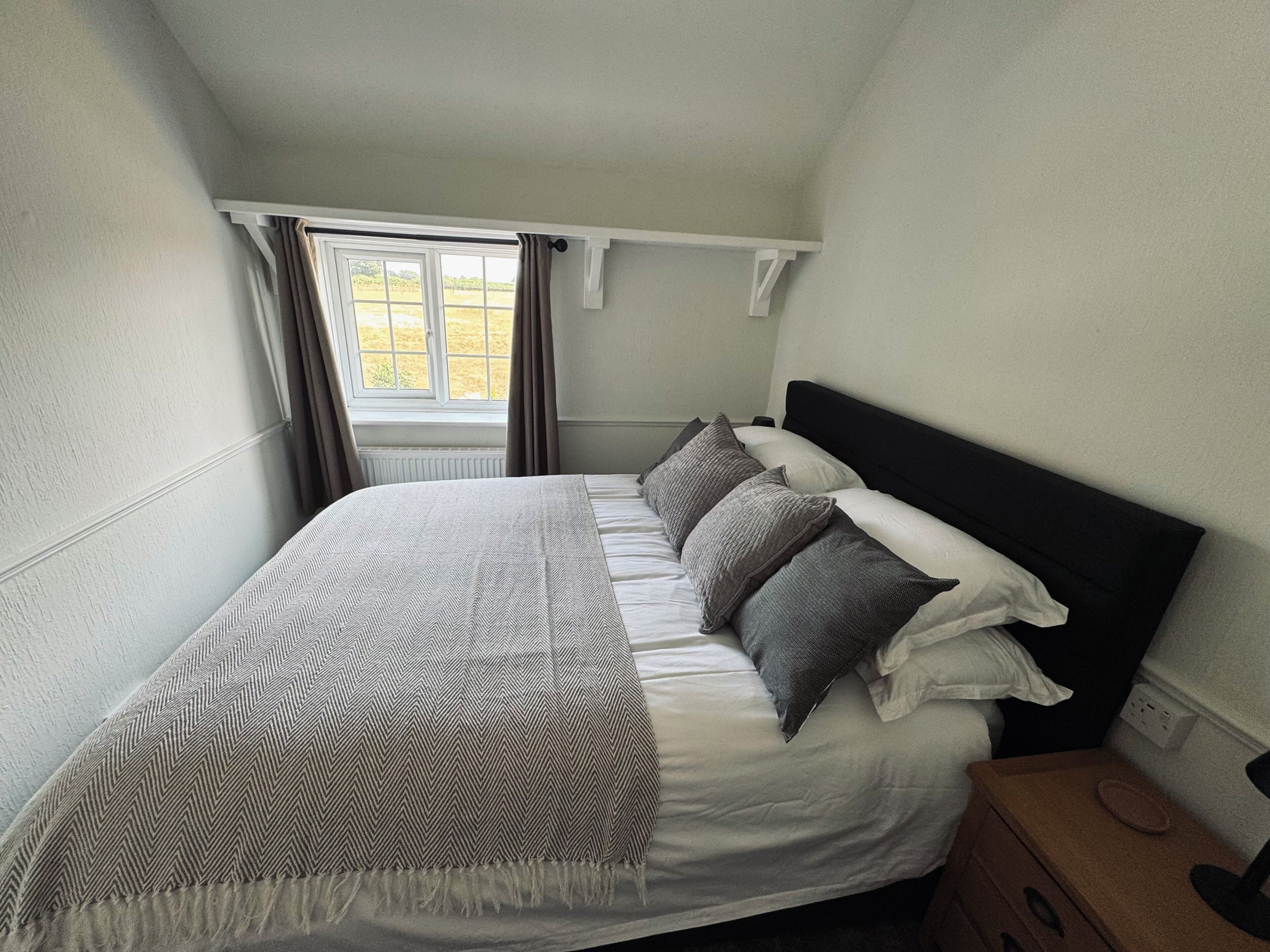 A bedroom with a bed, a window with curtains, a bedside table, and a nightstand.