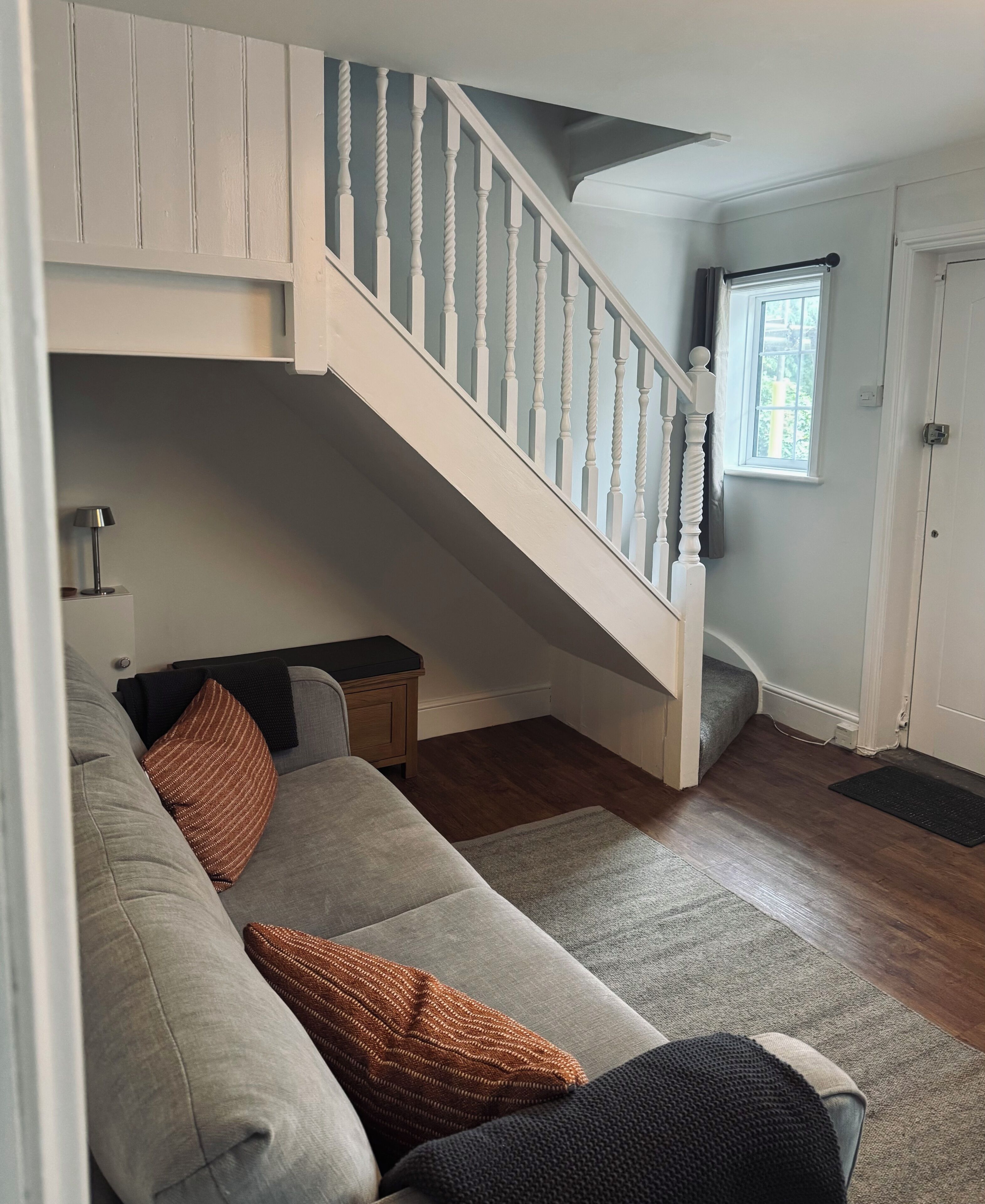 A living room with a staircase, a sofa, a lamp, and a window.