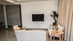 Ett modernt vardagsrum med en platt-TV som är monterad på väggen, en soffa, två fåtöljer och ett litet träbord med en växt.