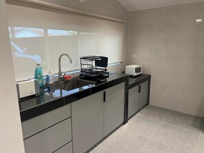 Uma cozinha moderna com bancada preta, pia, micro-ondas e cesto de arame preto.