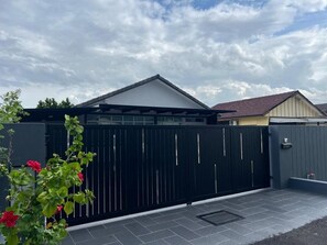 Una zona residencial cerrada con entrada pavimentada y una casa con techo a dos aguas.