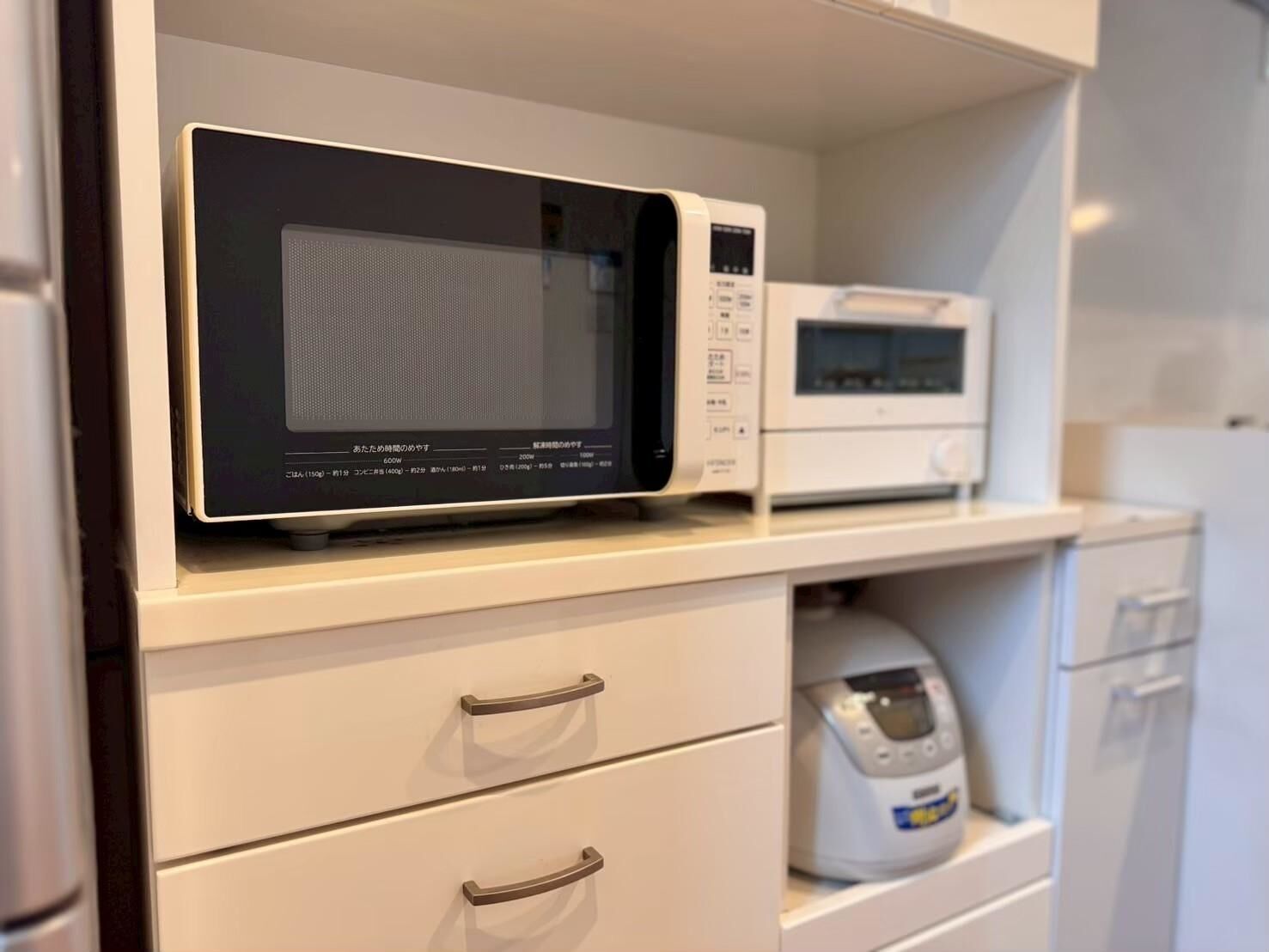 Un four à micro-ondes est posé sur une étagère blanche, au-dessus d’un tiroir, et un appareil électroménager blanc se trouve en dessous.