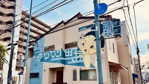 A building with a mural of a cartoon character, a blue sign indicating a pedestrian and bicycle path, and a street with a sidewalk and a parked bicycle. - 10 minutes from Okayama Station | Exclusive use for one group | Groups welcome | Up to 6 guests | 1 parking space | Loft | 1 restroom | Long-term stays welcome (岡山市)