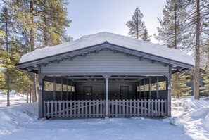 Un pavillon abrité, entouré d’une clôture en bois peinte en blanc, et bordé de neige et d’arbres.