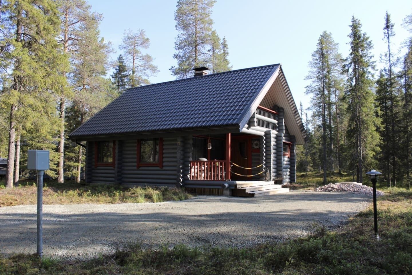 Hirsimökki, jossa on kuisti, ja sen ympärillä on metsää.