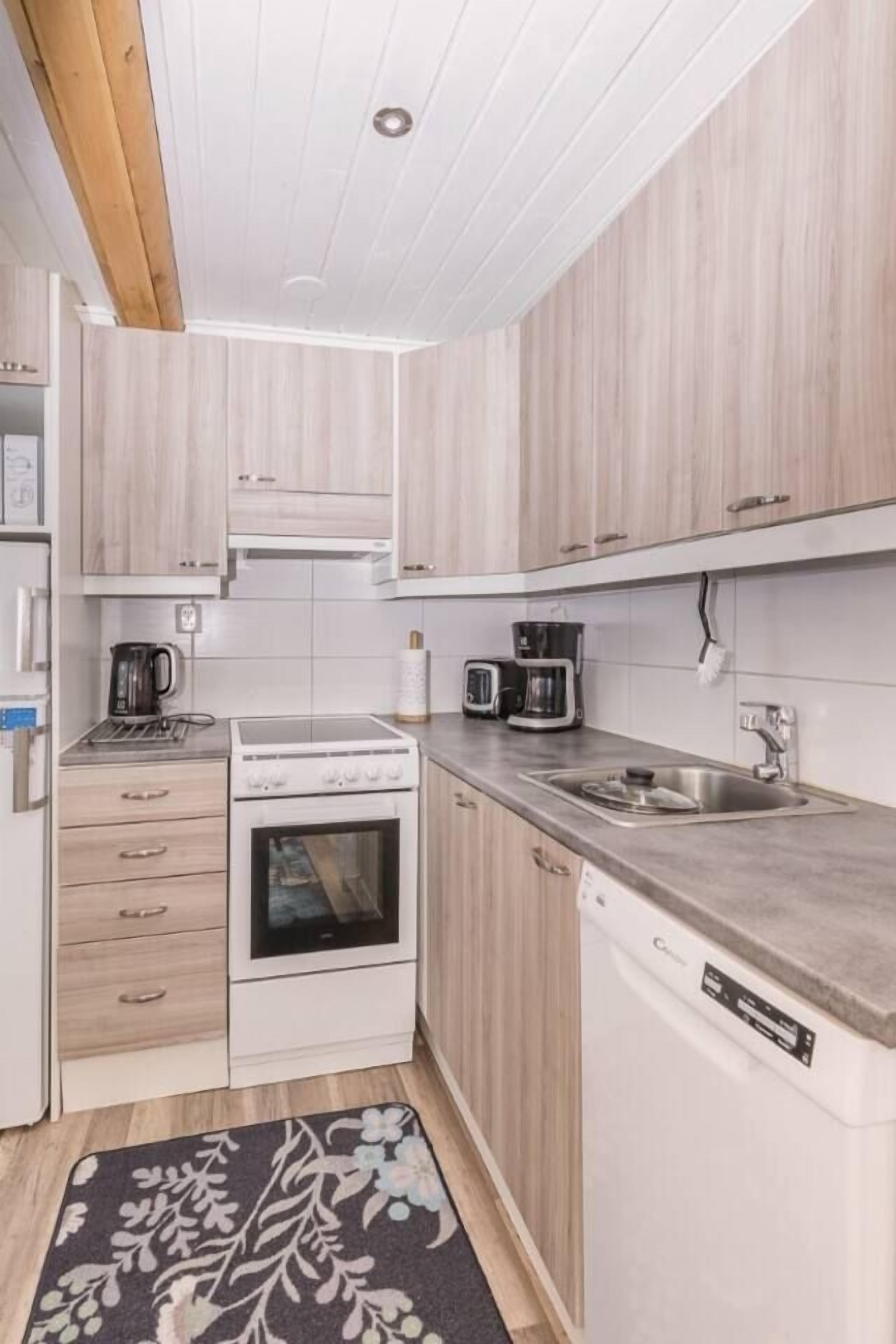 Kompakti keittiö, jossa on valkoiset kaapit, sisäänrakennettu uuni, astianpesukone ja kahvinkeitin.
