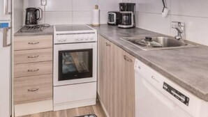A compact kitchen with white cabinets, a built-in oven, a dishwasher, and a coffee maker. - Onnela 1 Chalet | Sauna & Ski Trails | Ruka (Kuusamo)