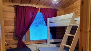 Una camera in una baita di legno con letti a castello, una scala, una finestra con tende e una lampada a soffitto.