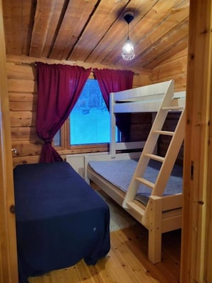 Une pièce de cabane en bois avec des lits superposés, une échelle, une fenêtre avec des rideaux et un luminaire au plafond.