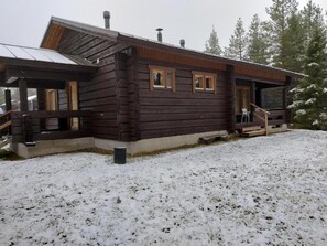 Eine Holzhütte mit Veranda, Schornstein und verschneitem Gelände.