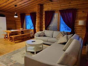 A cozy log cabin interior with a sofa, a round coffee table, a dining table, and a lamp.