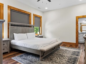 Ein Schlafzimmer mit einem Bett, Nachttischen, einem hölzernen Kopfteil, einem Fenster und einem Spiegel.