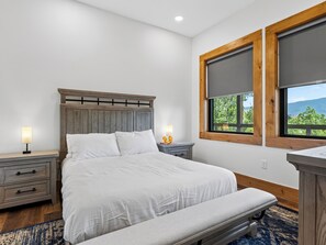 A bedroom with a bed, bedside tables, a bench, and a window with a view. - Sleeps 40 + 2 Indoor Pools + Game Rooms | The Spurling Collection (Sevierville)