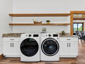 A laundry area with two front-loading washing machines, wooden shelves above, and a view of the outdoors through a glass door. - Sleeps 40 + 2 Indoor Pools + Game Rooms | The Spurling Collection (Sevierville)